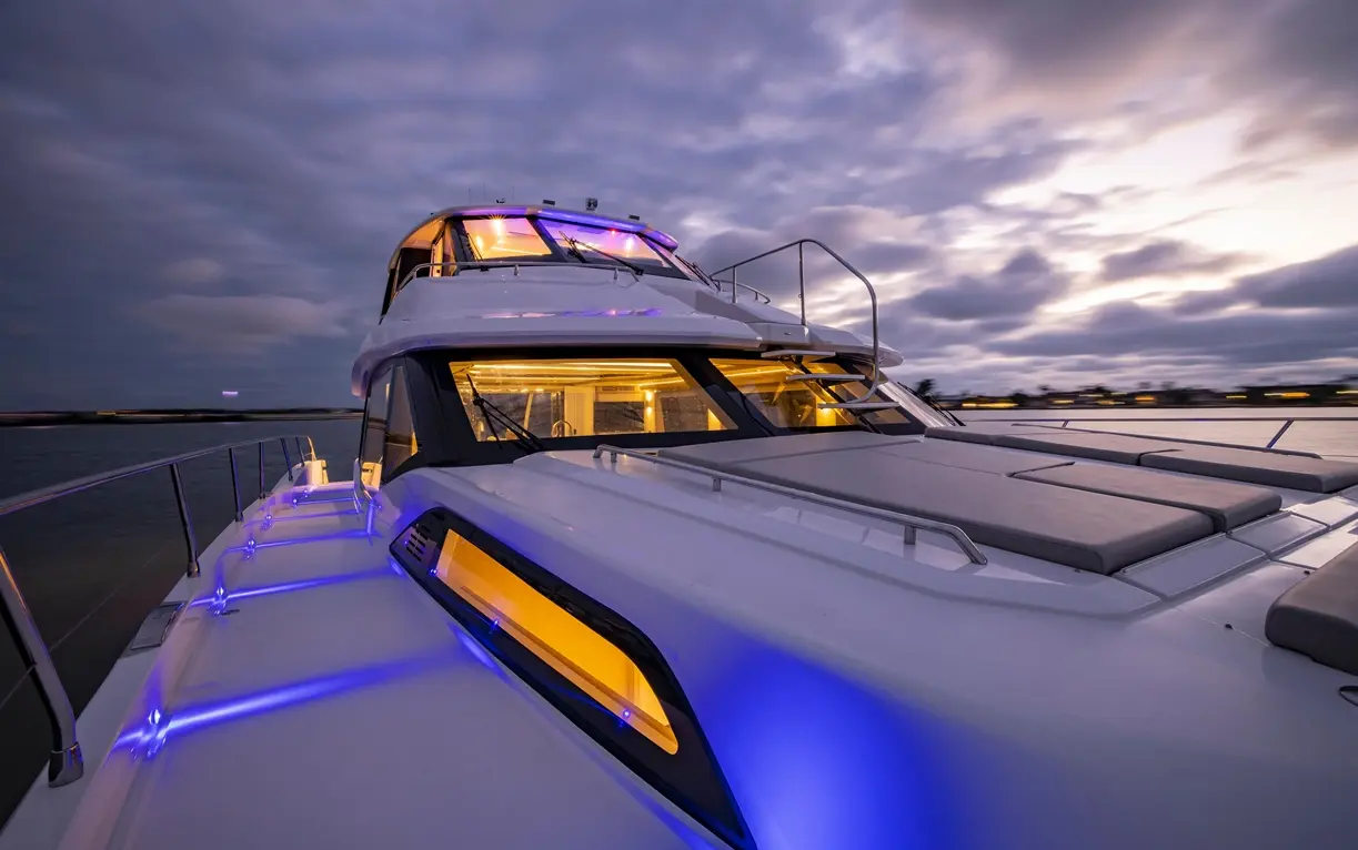 Luxury yacht deck illuminated by blue lights, with a view of a cloudy twilight sky and water in the background.